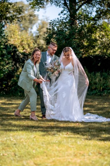 Freie Rednerin lacht gemeinsam mit einem Brautpaar im Garten während der Trauzeremonie.