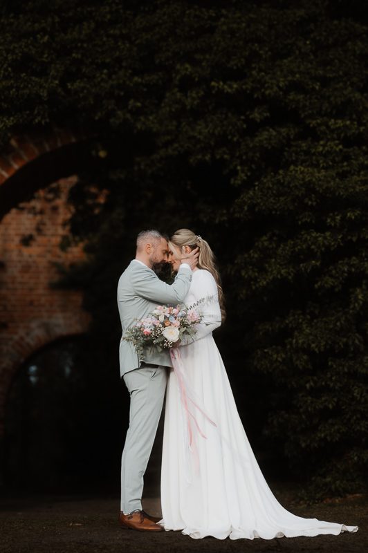 Ist das „Traumpaar“ ein Mythos? Brautpaar steht im Freien. Er drückt sie mit seiner rechten Hand ihren Kopf an seinen, so dass sich Stirn und Nase berühren.