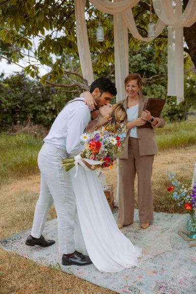 Brautpaar küsst sich während der Trauung, freie Rednerin steht lächelnd daneben.