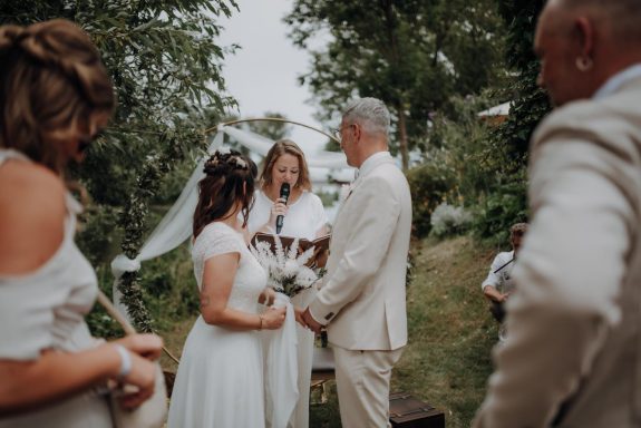 Traurednerin spricht ins Mikro, Brautpaar blickt zur Rednerin